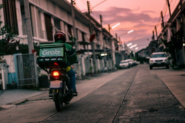 A person rides a motorcycle down a narrow street at sunset, with buildings on both sides.