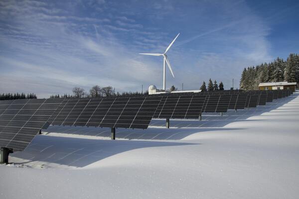 Solar panels on snow with windmill under clear day sky