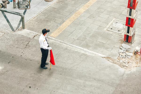 A security guard standing on the street, holding a red flag.