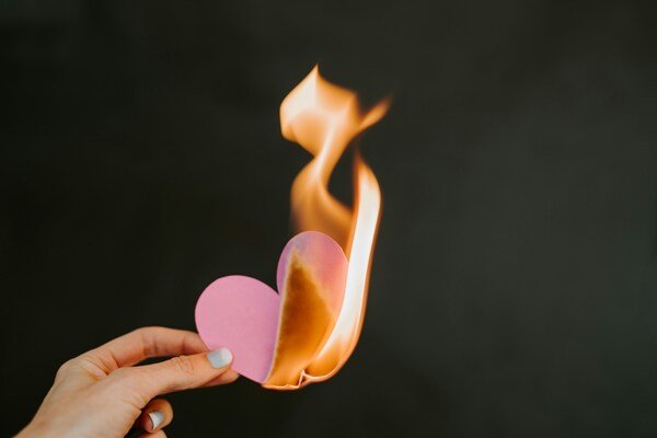 Person holding a paper heart in front of a fire