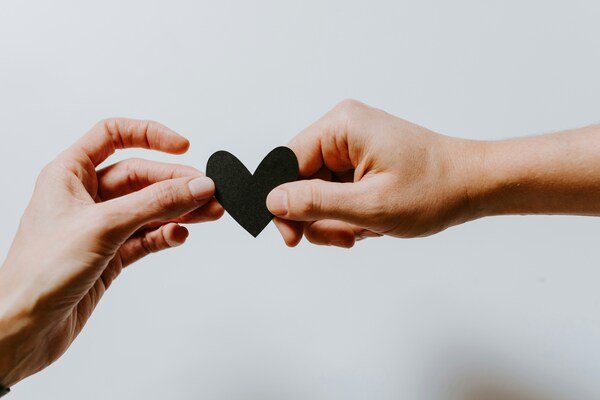 Two people holding a paper-cut heart together