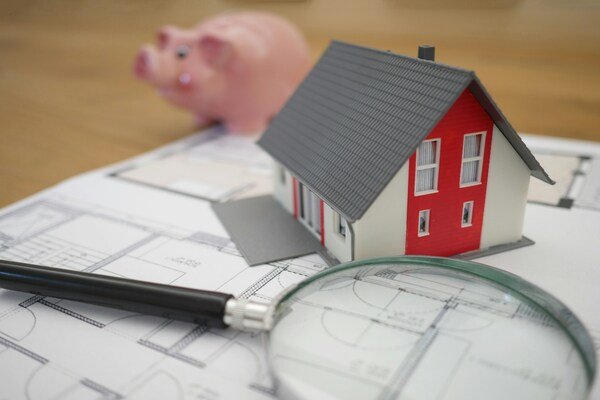 White and red miniature wooden house next to a grey-framed magnifying glass
