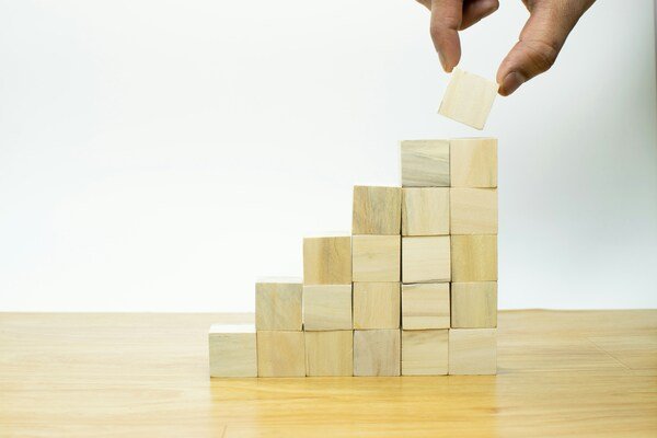 A person placing a piece of wood into a wooden pyramid structure.
