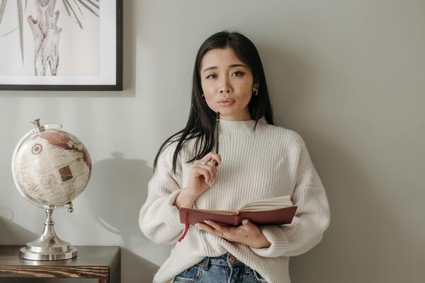 Woman in a white knit sweater holding a notebook and pencil