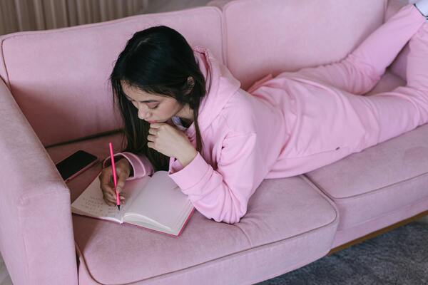 Woman in pink clothes lying on the couch while writing in a notebook