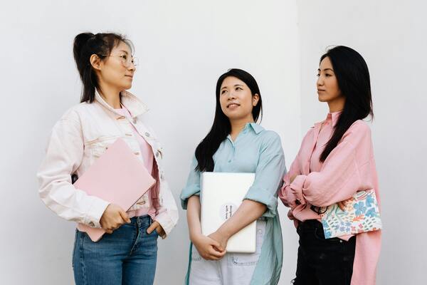 Three women standing together, holding a laptop and a notebook