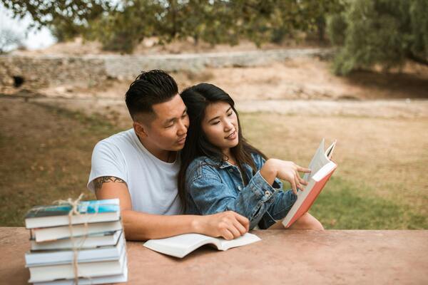 A couple sitting together in a park, reading a book.