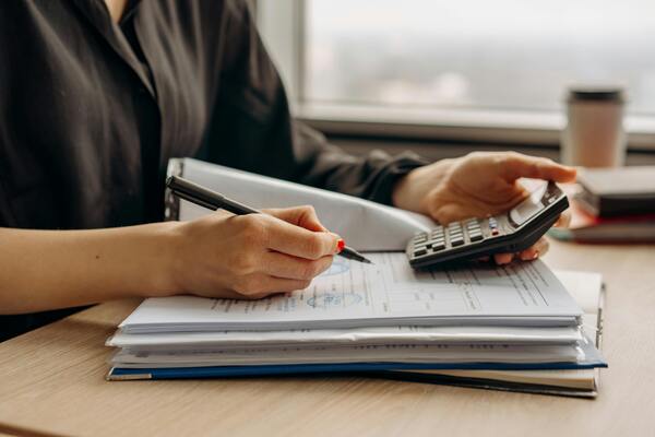 A person holding a calculator and writing in a notebook