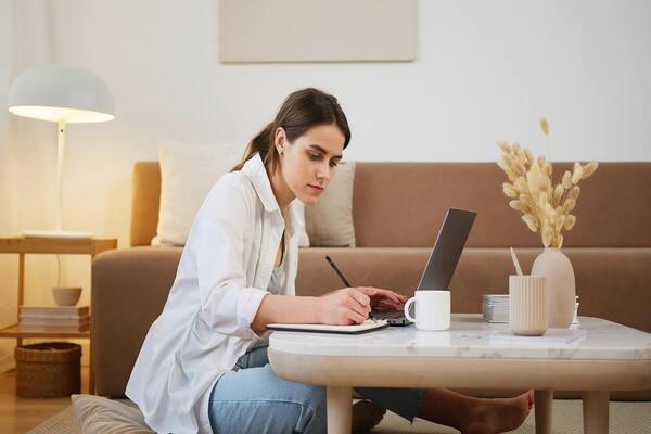 A young woman uses a laptop and takes notes.