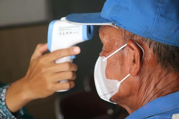 Person measuring temperature of an old man in blue cap by thermometer gun