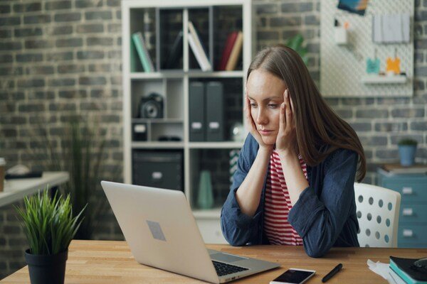 A woman sitting and facing a laptop with hands on her face