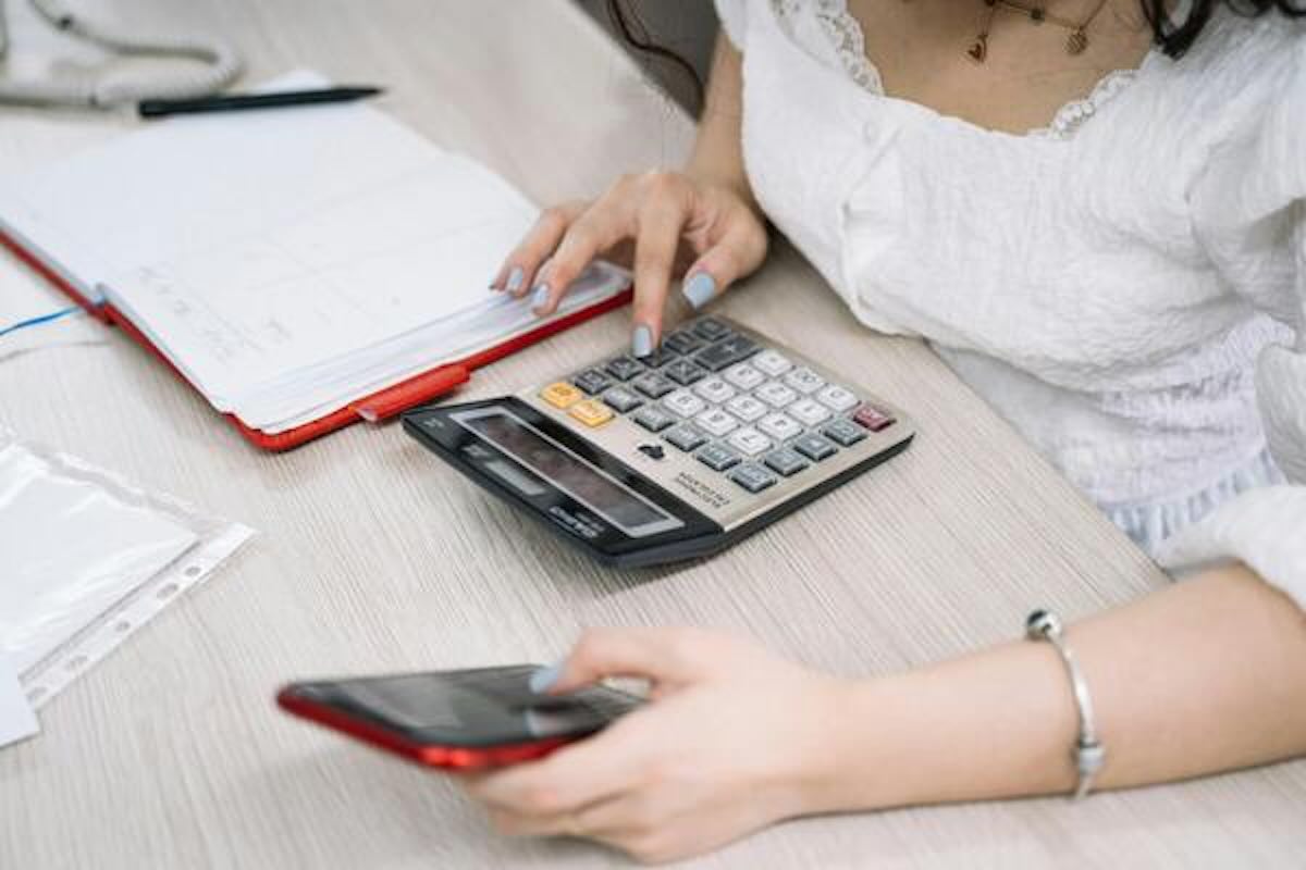 Woman reviewing expenses with a calculator and smartphone while considering advice from a financial advisor for budgeting.
