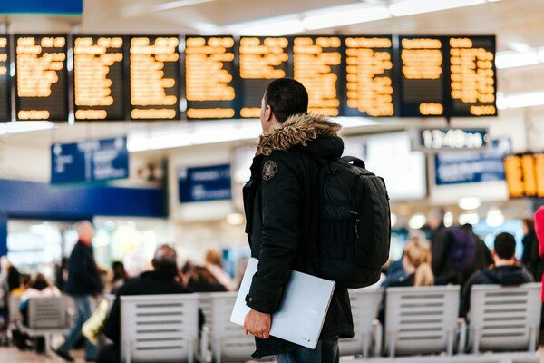 A man standing in the centre of airport looking at the LED flight schedule bulletin board