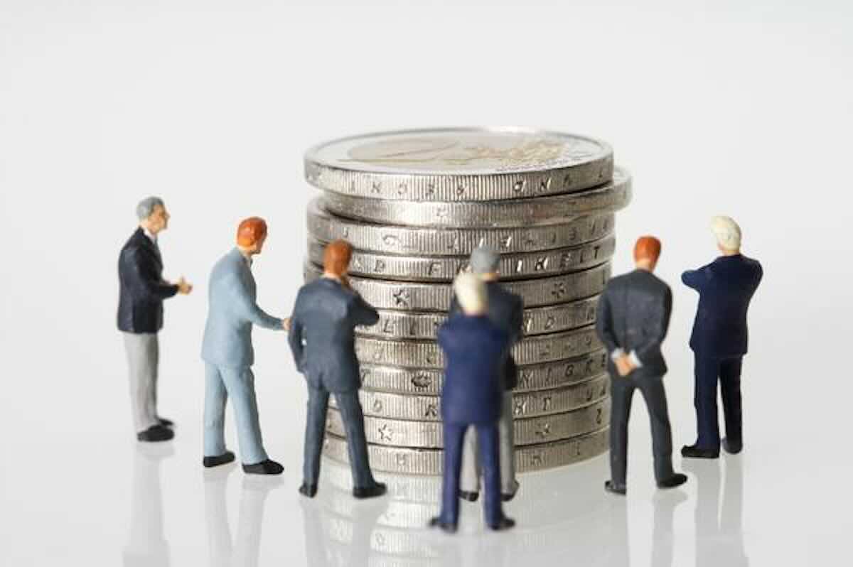 Miniature business figures gathered around stacked coins, representing retirement savings and the SRS and tax deadline.
