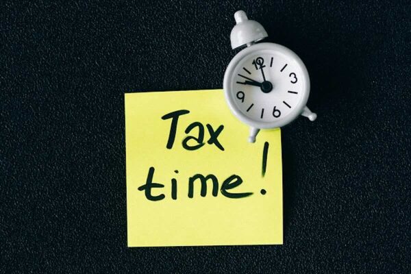 Sticky note reading "Tax time!" beside an alarm clock, reminding taxpayers to prepare before the SRS and tax deadline.