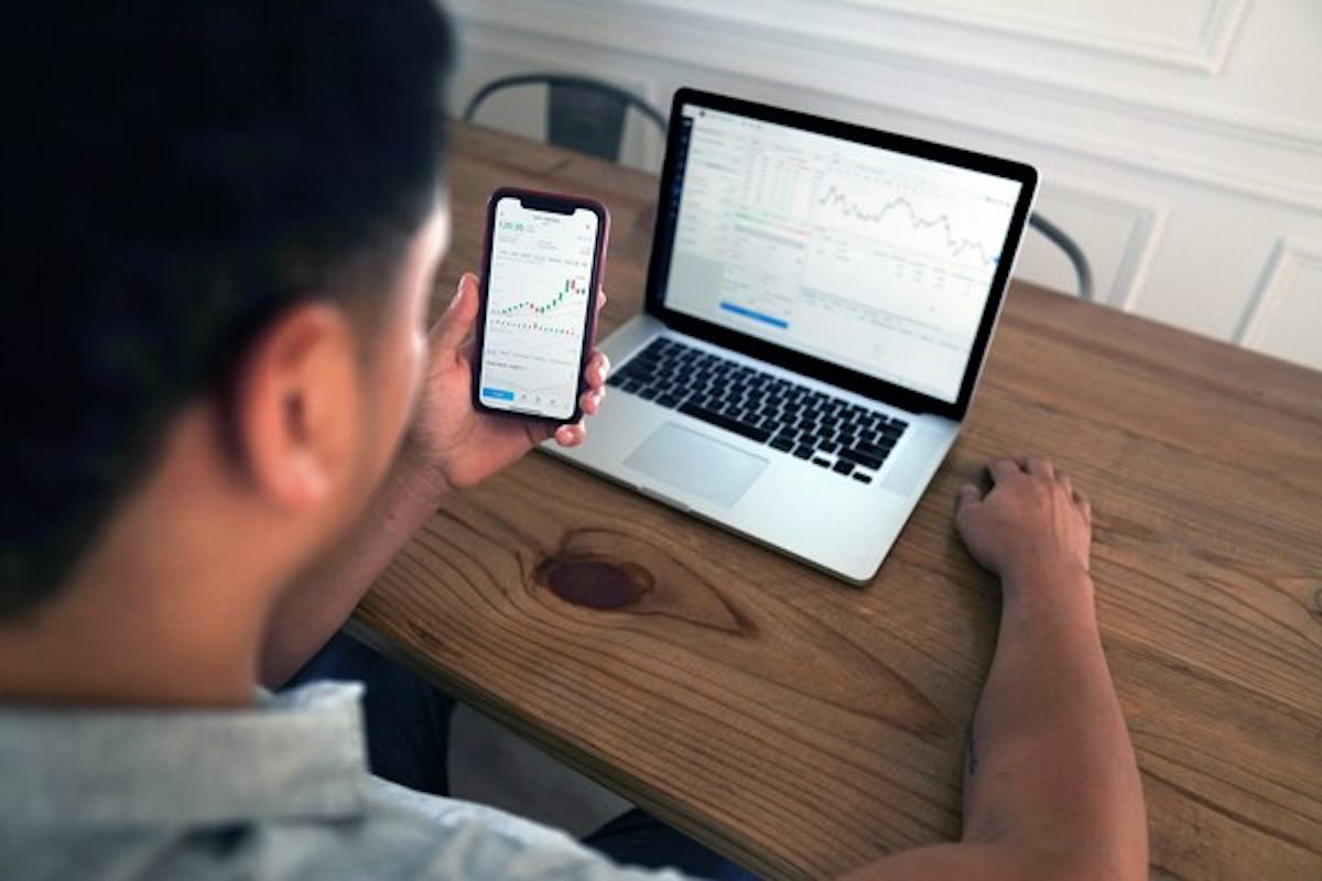 Investor reviewing market charts on a smartphone and laptop while researching short duration bond funds for stable income.