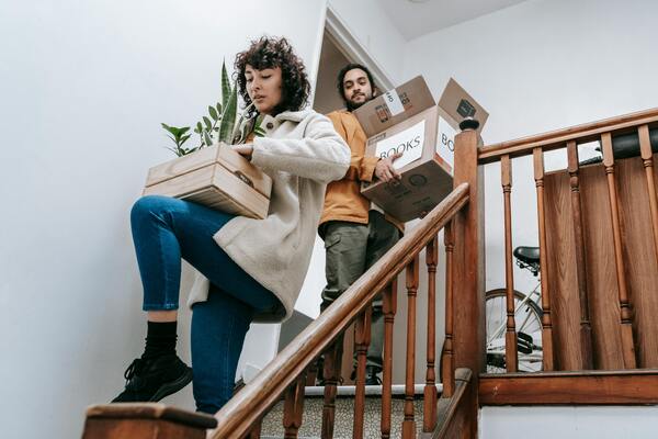 Two people carrying boxes and plants downstairs