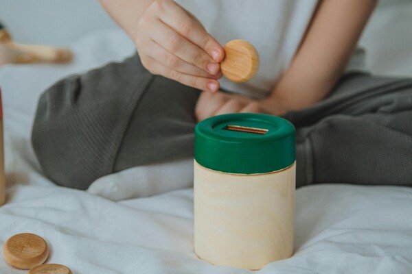 A child putting toy wooden coin in a wooden saving bank