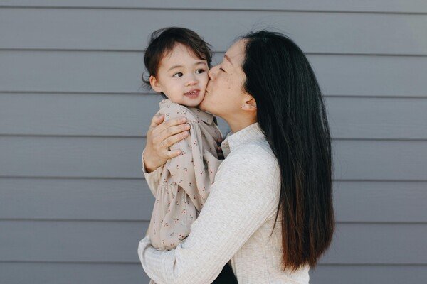 A woman carrying a little girl and kissing its head
