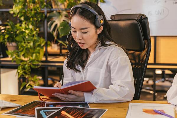 Young professional wearing a headset taking notes at a desk, representing remote work, job training, and career development support.