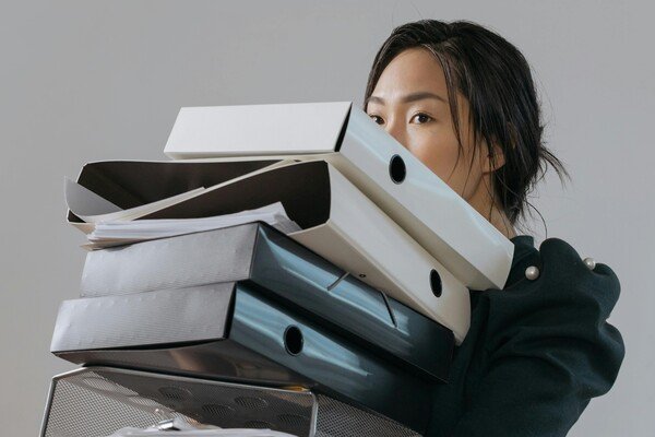 Office worker carrying a stack of files and folders, representing work stress, job pressure, and administrative burden.