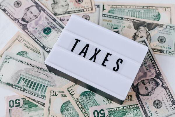 Word “TAXES” on a lightbox surrounded by US dollar bills, illustrating taxation, income planning, and financial obligations.