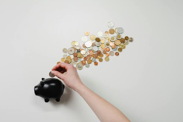 Hand placing coins into a piggy bank on a white background, representing saving money, financial planning, and long-term goals.