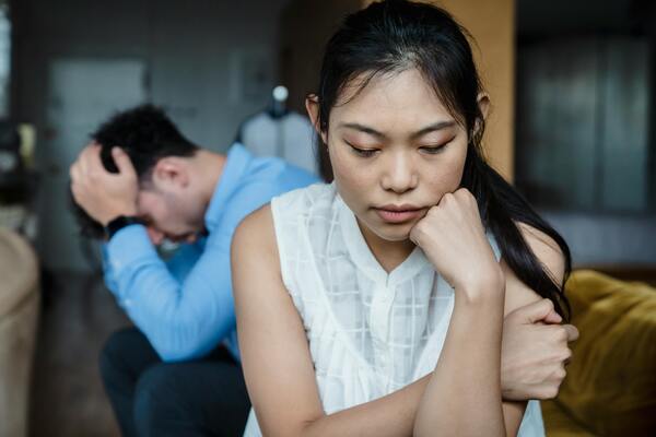 Young couple sitting apart looking worried, symbolizing financial stress, money problems, and relationship strain.