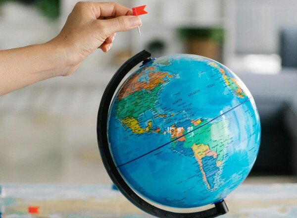 Hand placing a red pin on a world globe, representing global markets, geopolitical risk, and international investment exposure.