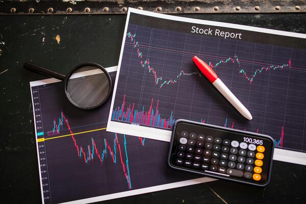 Stock market reports with price charts, calculator, and pen on a desk, representing investment research, risk analysis, and portfolio planning.