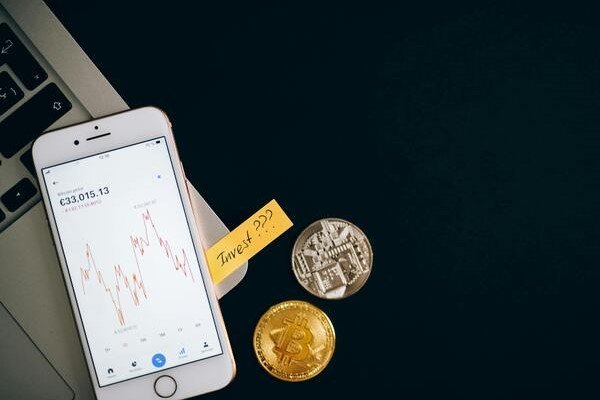 Smartphone showing a price chart beside cryptocurrency coins, symbolizing crypto investing, digital assets, and market speculation.