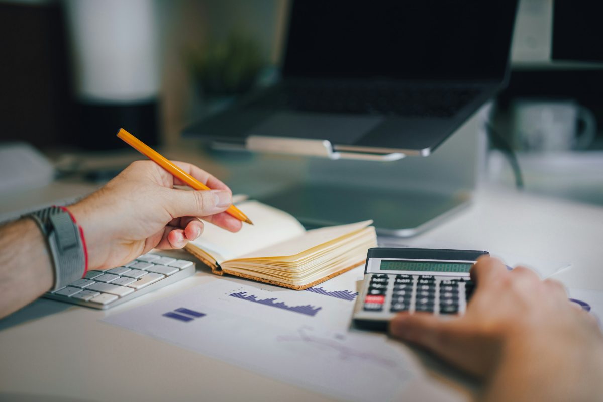 Person calculating expenses with a calculator and notebook at a desk, illustrating budgeting and financial planning