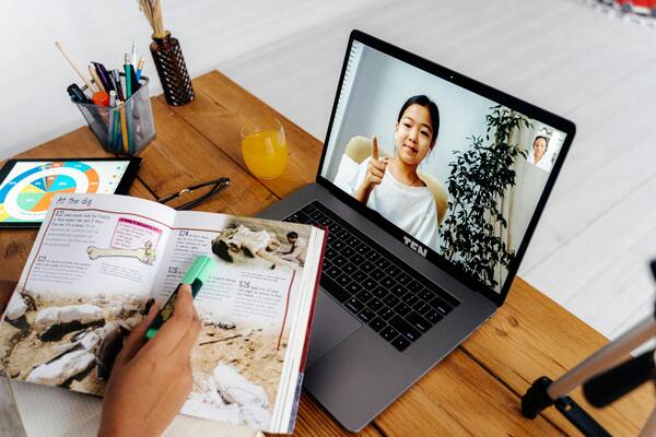 Student attending an online class on a laptop with study materials and notebook on a desk.