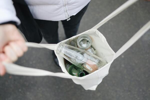 Person carrying a reusable shopping bag with glass bottles promoting sustainable and cost-saving habits.