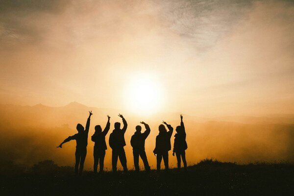 Silhouetted group of friends celebrating together outdoors at sunset during a group trip.