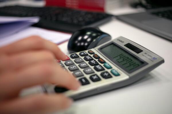 Hand using a calculator to estimate insurance costs and travel expenses for trip budgeting.