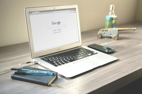 Laptop on a desk with Google search open, notebook and smartphone nearby, representing online research about IVF, fertility treatments, and egg freezing costs.