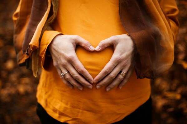Pregnant woman holding her belly with hands forming a heart shape, symbolizing pregnancy, fertility, and maternal care.