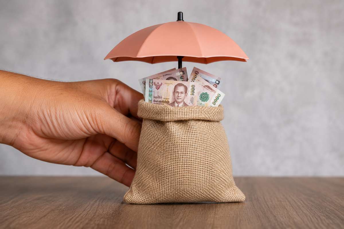 Hand protecting a money bag with cash under an umbrella symbolising health insurance or financial protection