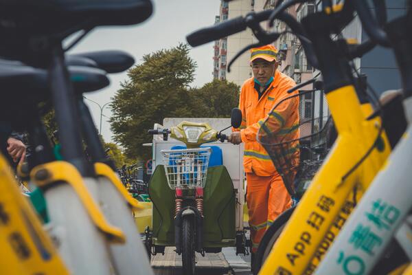 City worker in high-visibility uniform transporting shared bicycles for urban mobility services.