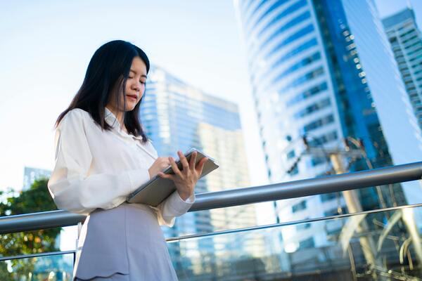 Professional Asian woman using tablet in modern city, midlife career transition and digital skills development concept.